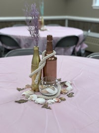 a table setting with two bottles and seashells on a pink tablecloth